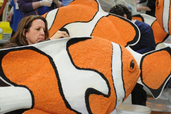 Woman decorating large fish float with orange and white flowers