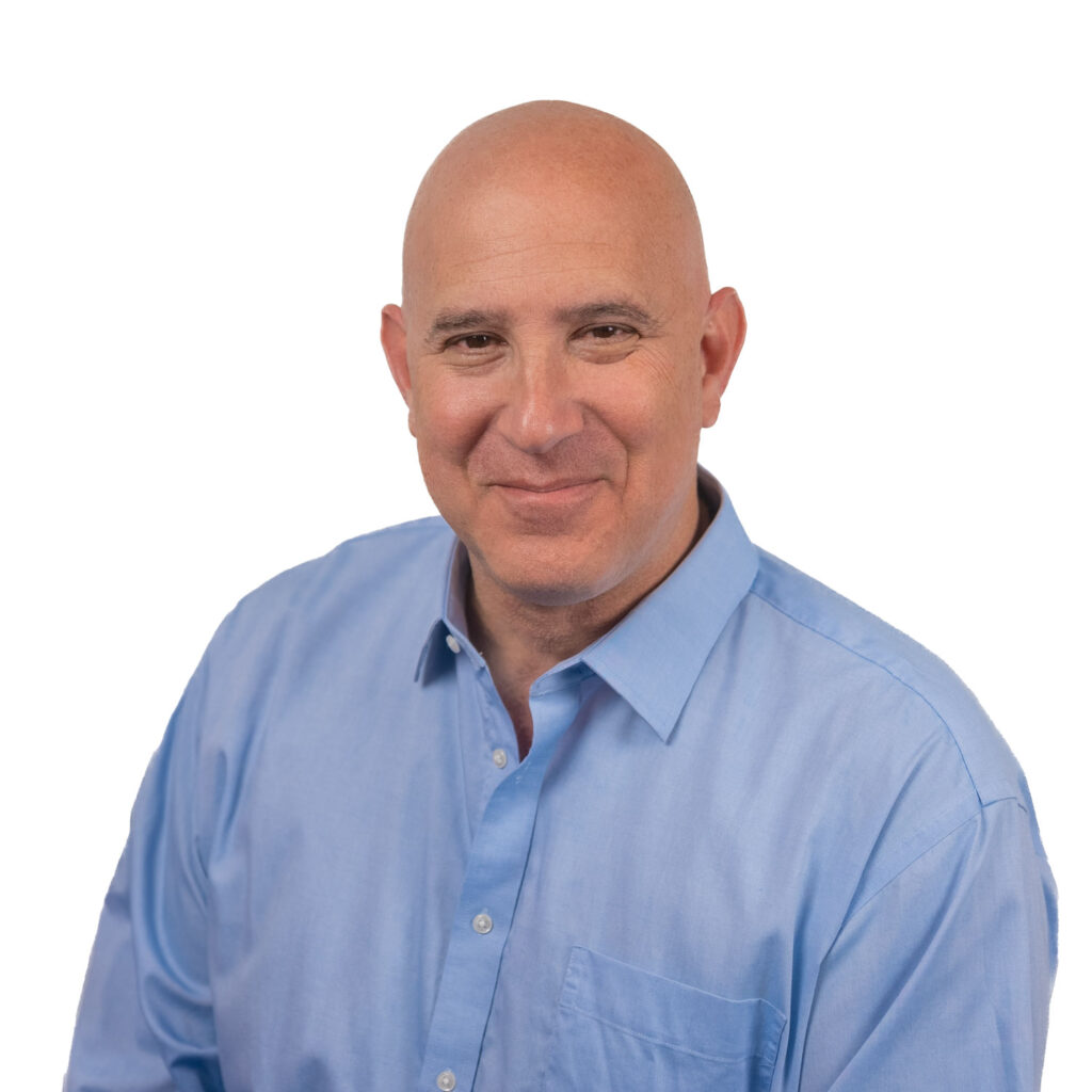 Stefan_Full-20230613 Man in light blue shirt smiling against a white background.