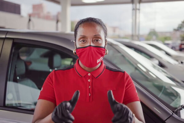 Car rental employee in red uniform and mask standing by vehicles