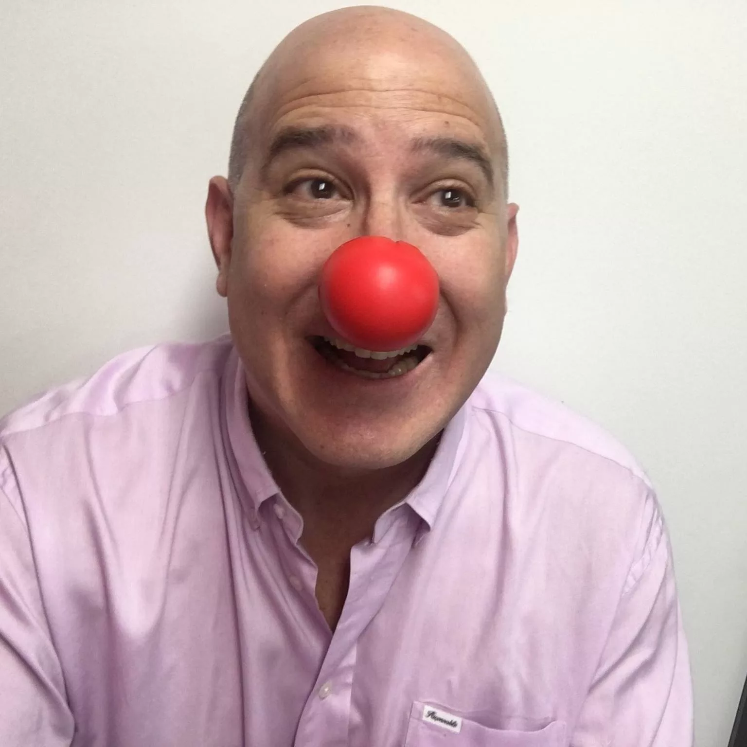 Man in pink shirt smiling with a red clown nose