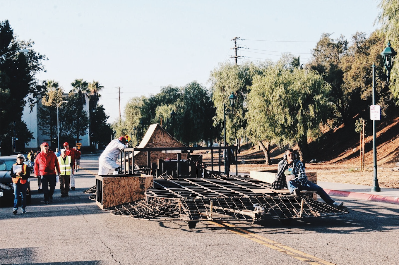 Workers assembling large metal framework on a sunny street with bystanders watching