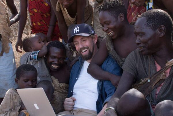 Man with laptop surrounded by joyful people in rural setting