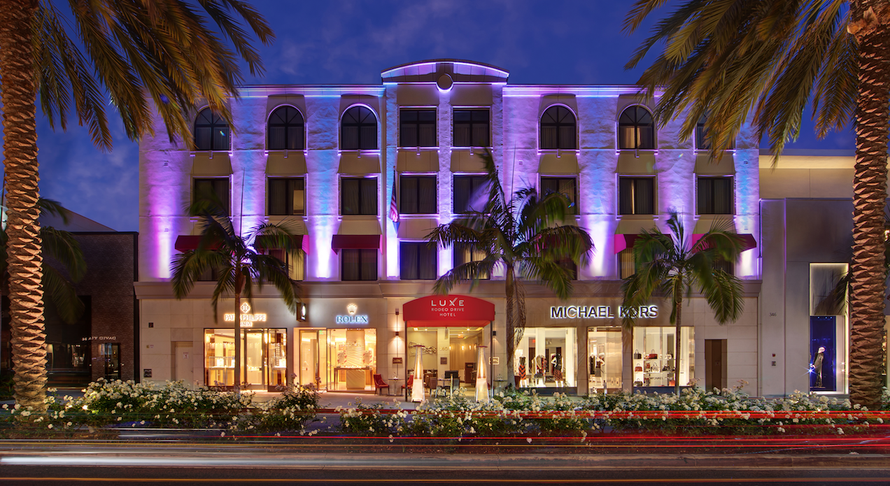 Illuminated luxury hotel facade at night with palm trees and upscale shops.