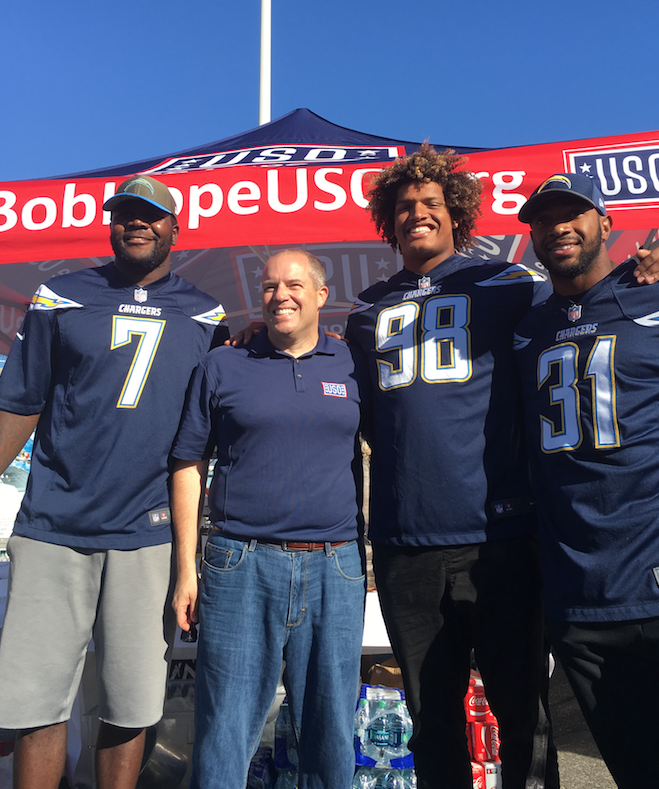 Three football players and a fan posing in front of a USO tent
