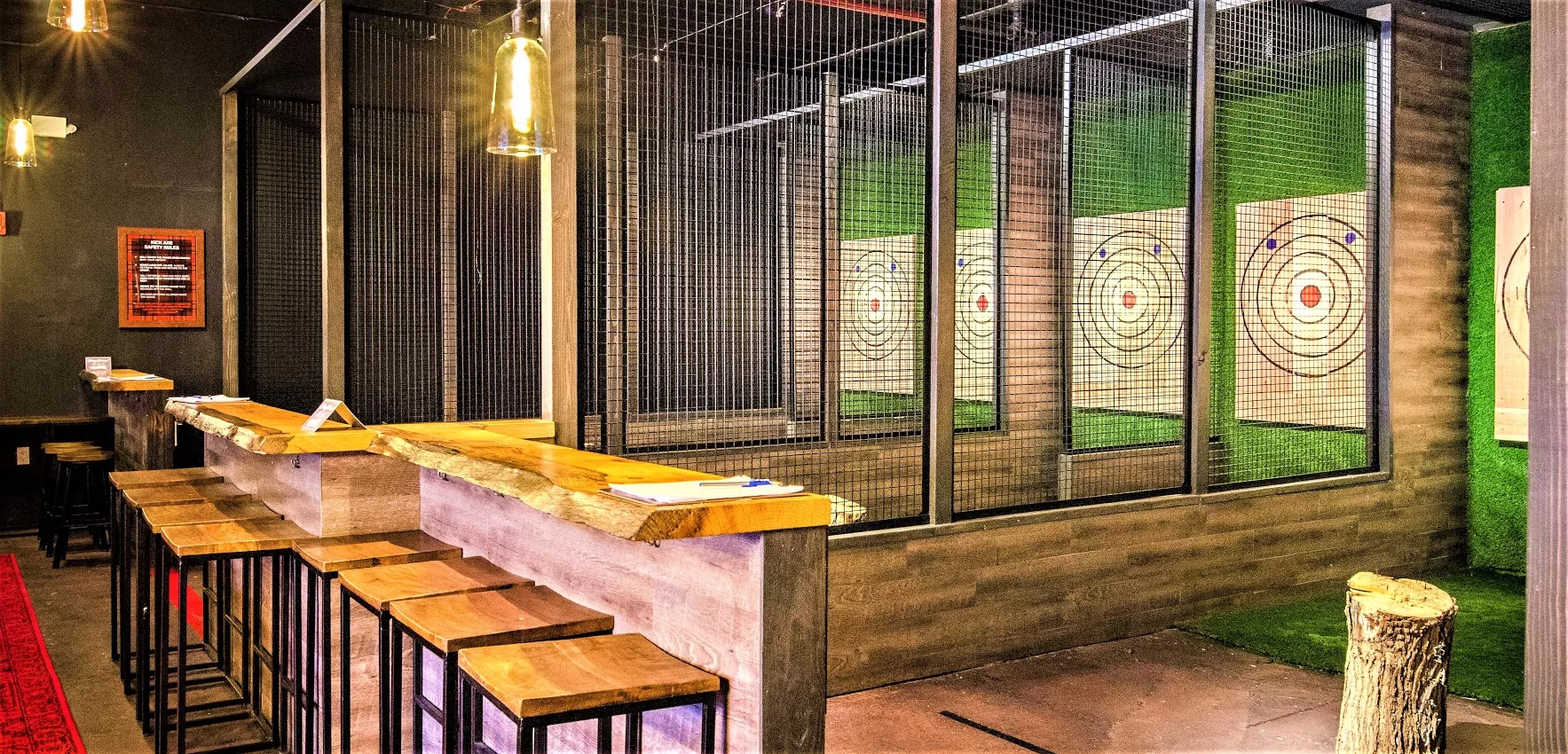 Indoor axe throwing lanes with target boards and bar stools.