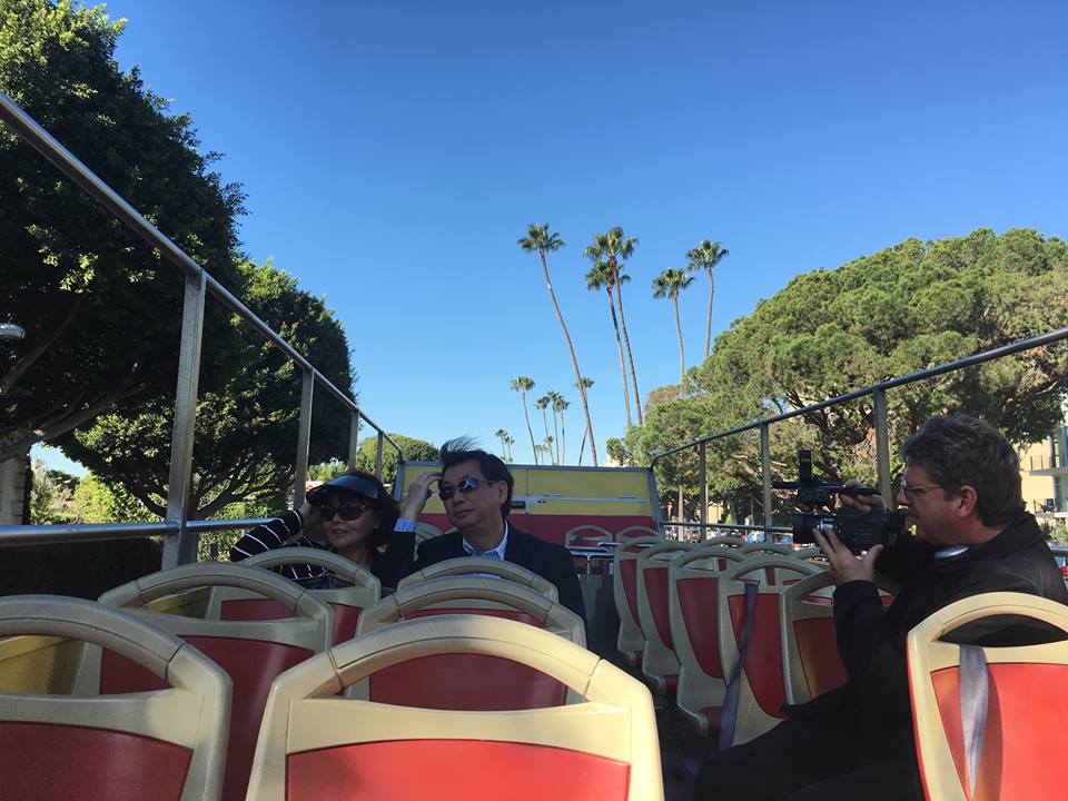 Tourists on a sightseeing bus tour with clear skies and palm trees in the background.