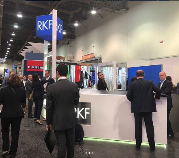 Professionals networking at RKF trade show booth with company signage.
