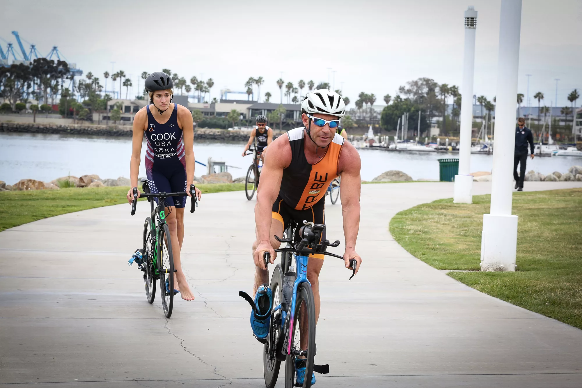 Two triathletes cycling on a path near the marina