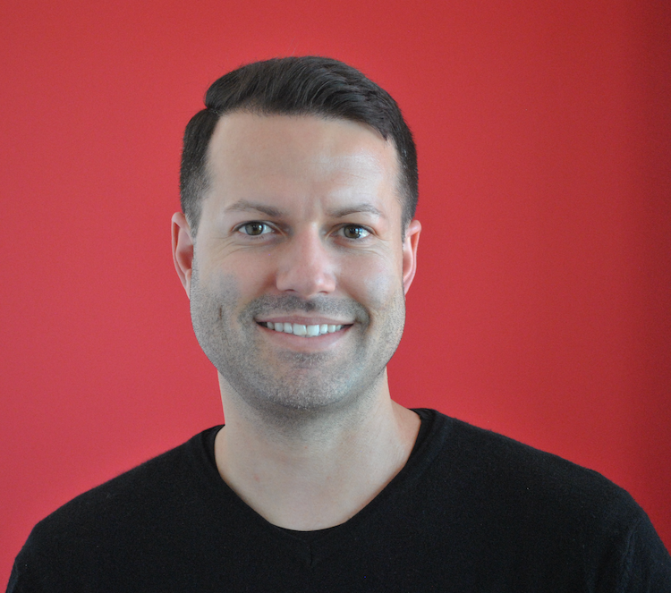 Man with a smile wearing black shirt against red background