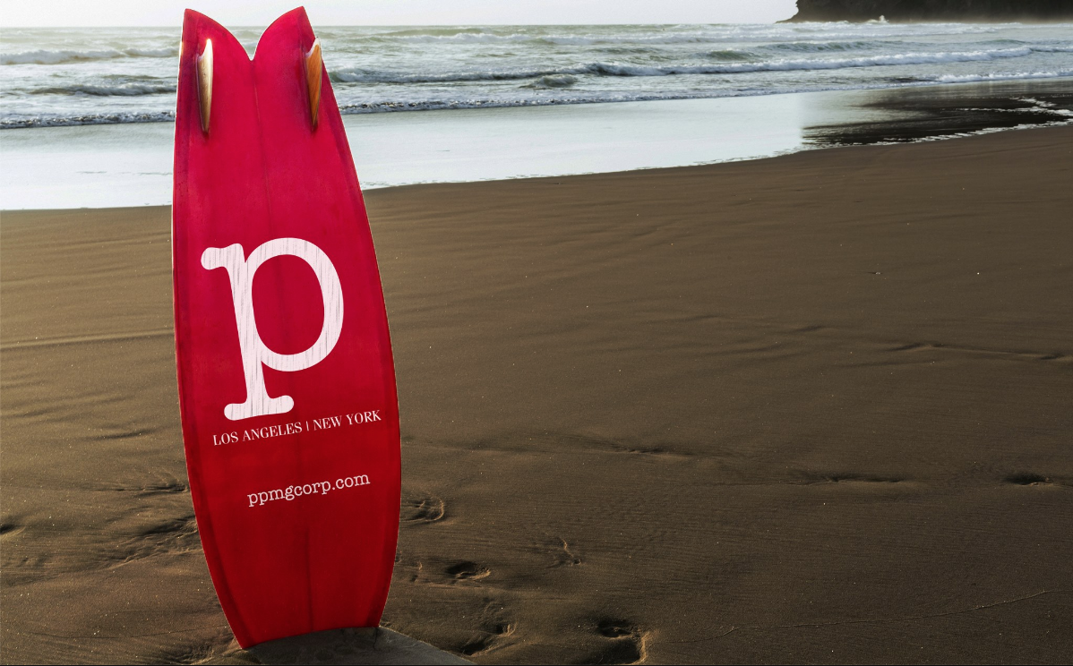 Red surfboard with logo standing on sandy beach with waves in background