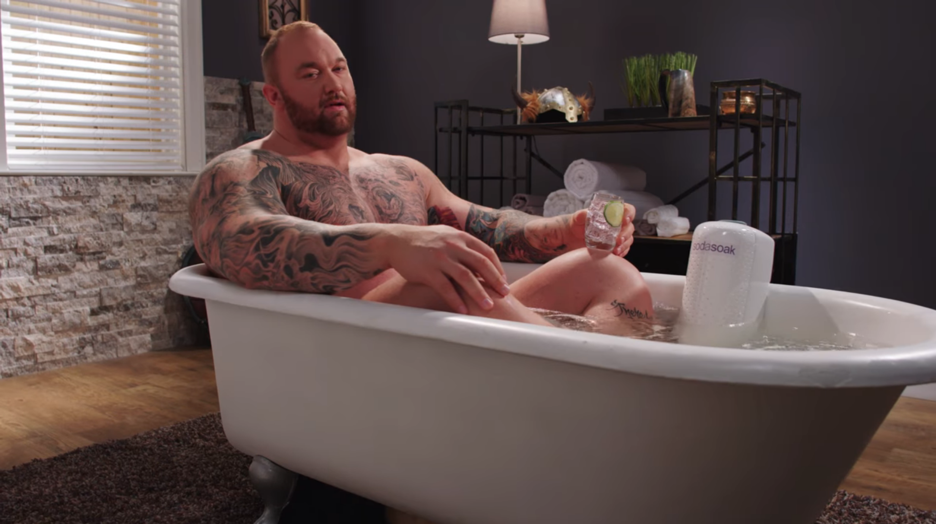 Tattooed man relaxing in a bathtub with a drink
