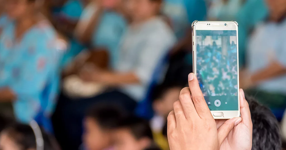 Person holding a smartphone with blurred audience in the background