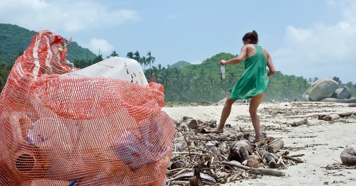 Woman cleaning beach debris with large red net bag