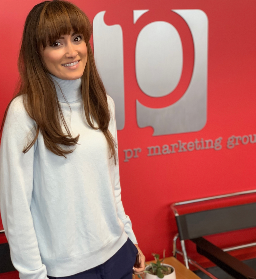 Woman in white sweater smiling in office with PR Marketing Group logo
