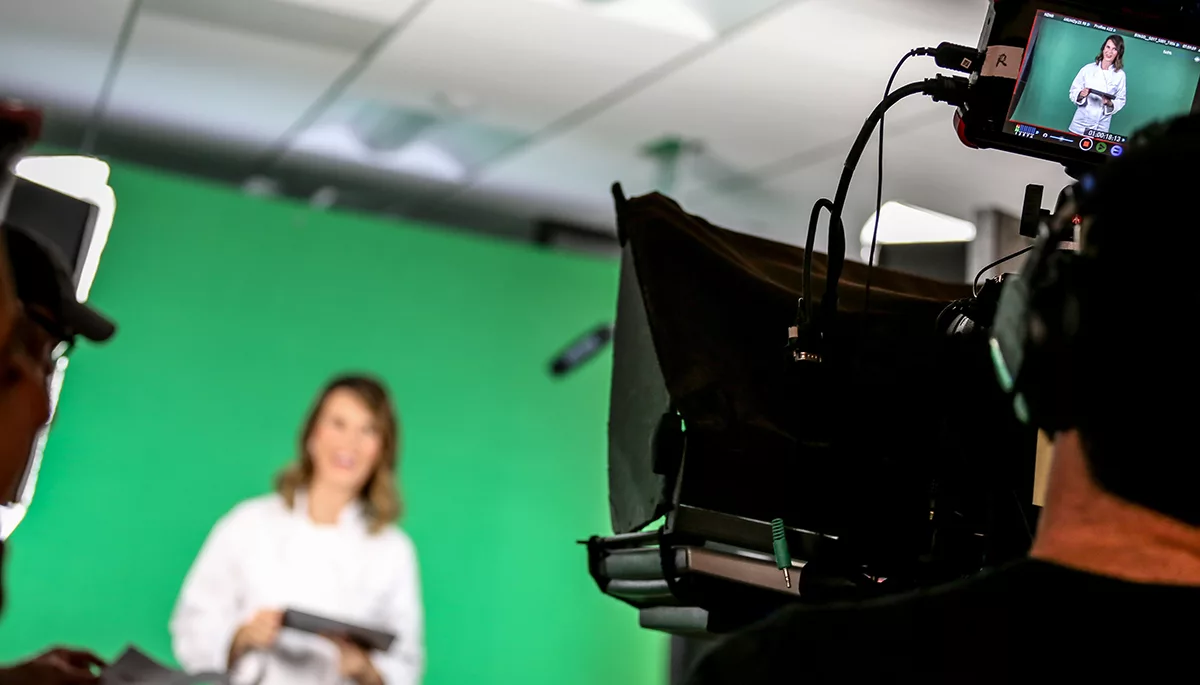 Woman with tablet in video production setup with green screen and camera equipment.