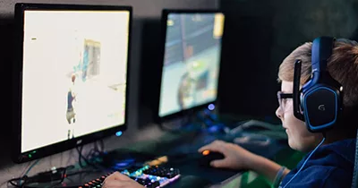 Teenager playing online game with headset and dual monitors