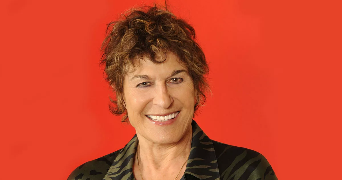 Smiling person with curly hair against a red background wearing a camouflage shirt