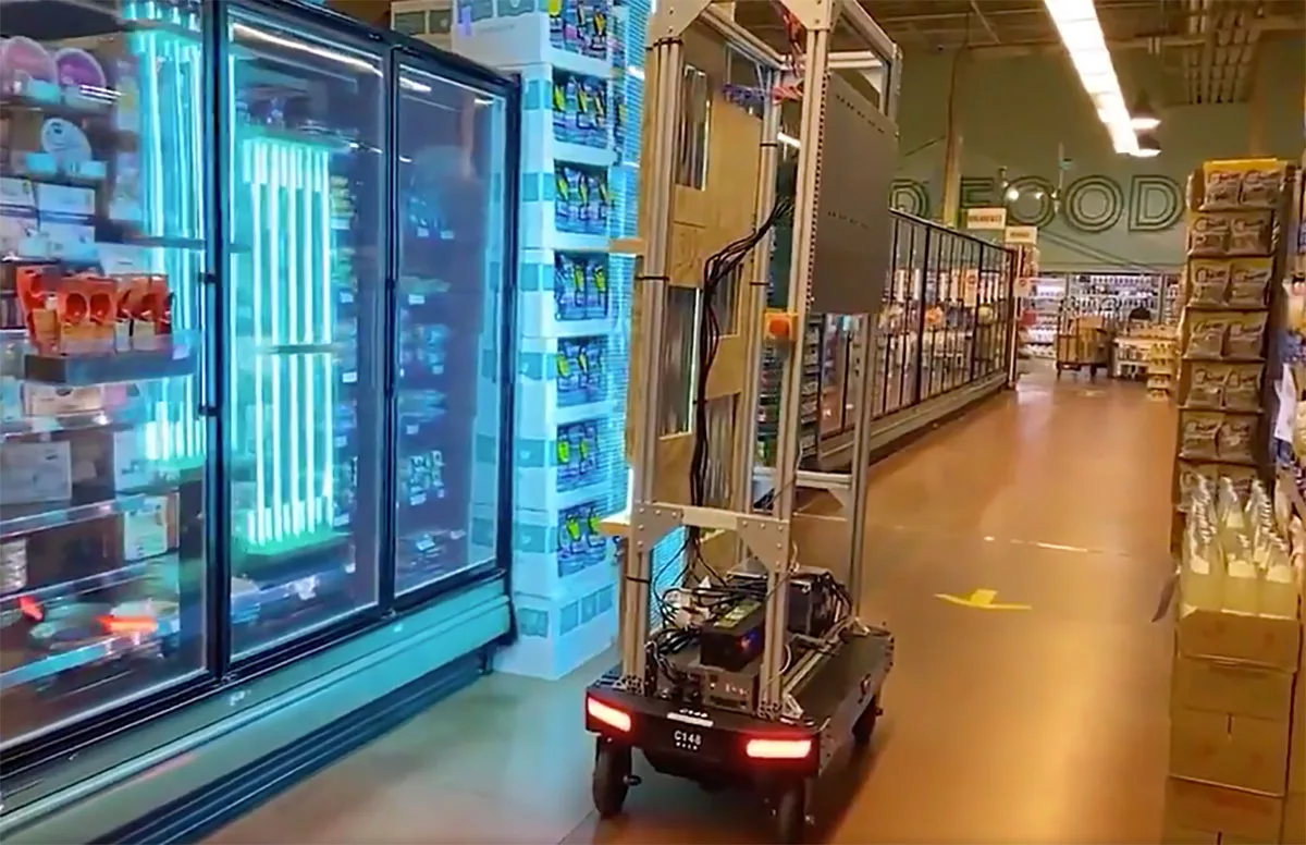Robot cart navigating a grocery store aisle near refrigerated section.