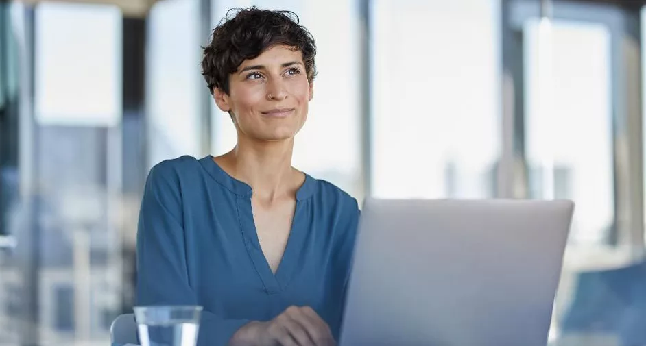 Professional woman smiling at office with laptop and city view.