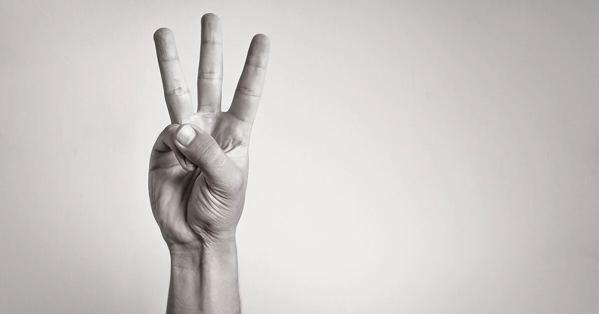 Hand showing three fingers up gesture on grey background