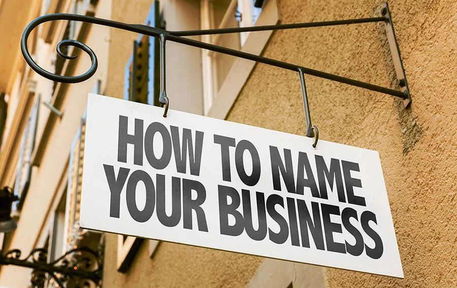 Sign reading "How To Name Your Business" hanging on a wrought iron bracket.
