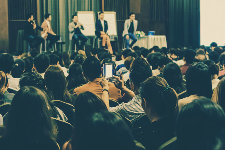 Audience attending a business seminar with a panel of speakers on stage