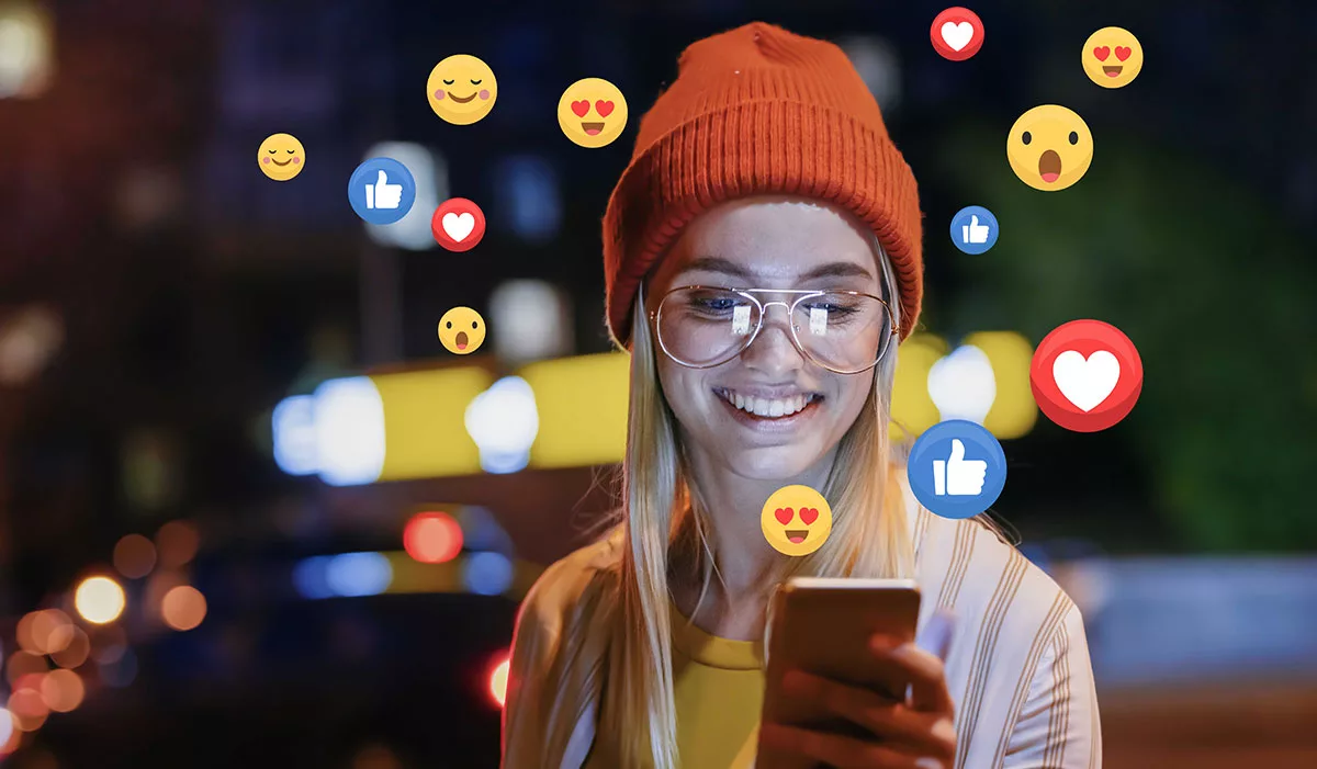 Smiling woman with glasses using smartphone with social media reactions floating around