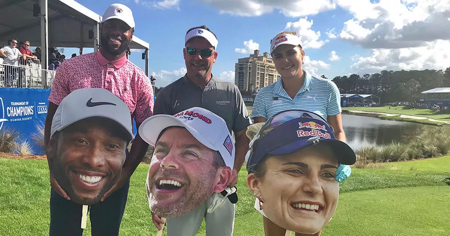Golfers holding oversized face cutouts at a sunny golf event.
