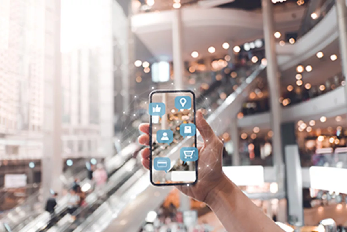 Hand holding smartphone with social media icons in a bustling mall interior