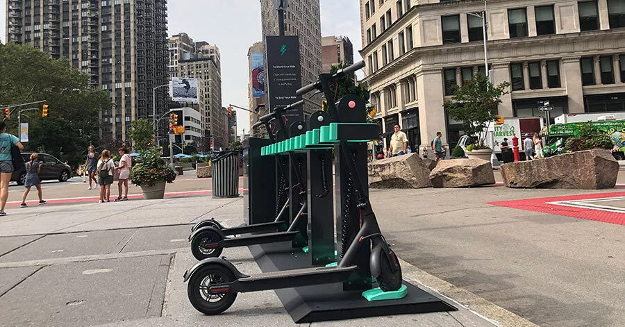 Electric scooter docking station on city street with pedestrians in background