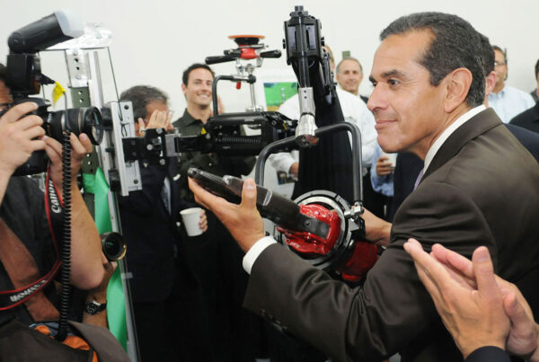 Man in suit interacts with robotic arm amidst photographers and onlookers.