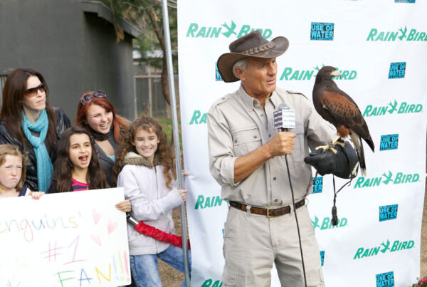 Man with hat holding microphone and falcon at outdoor event with spectators and signs