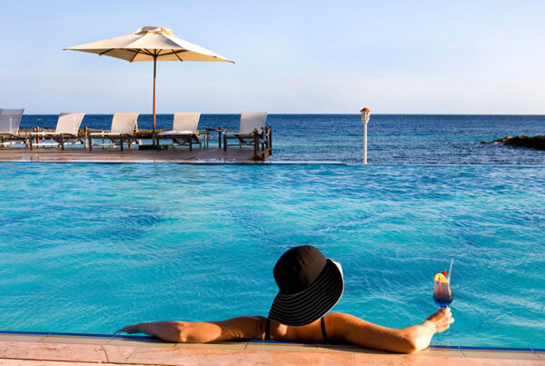 Woman relaxing by infinity pool overlooking ocean with sunbeds and umbrella