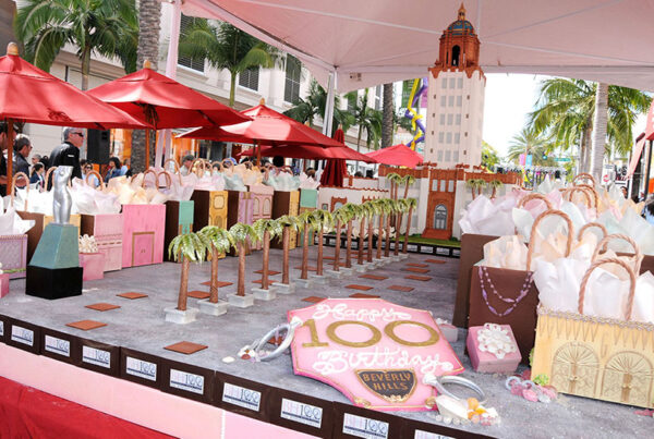 Outdoor Beverly Hills 100th birthday celebration with decorative cake and gift bags.