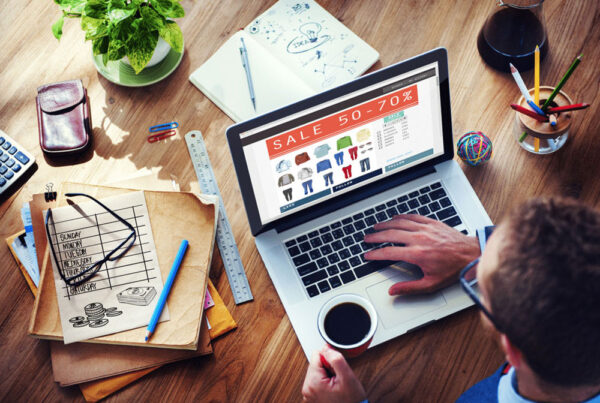 Person shopping online during sale event with coffee and design sketches on desk