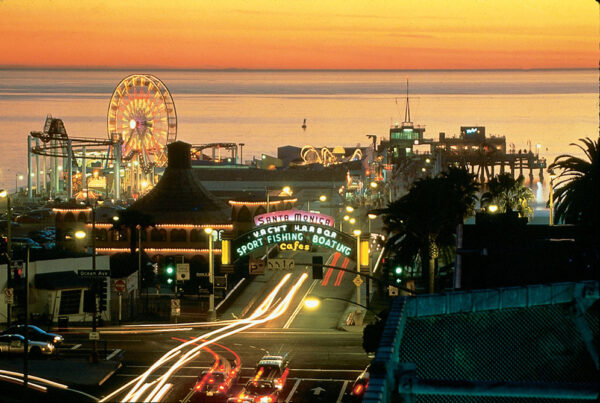 Sunset view of Santa Monica Pier with Ferris wheel and light trails from cars.