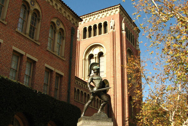 Historic brick university building with bell tower and statue in foreground