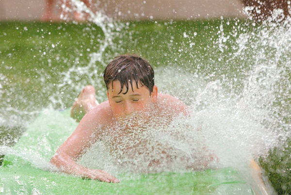 Boy splashing water while sliding on a green water slide