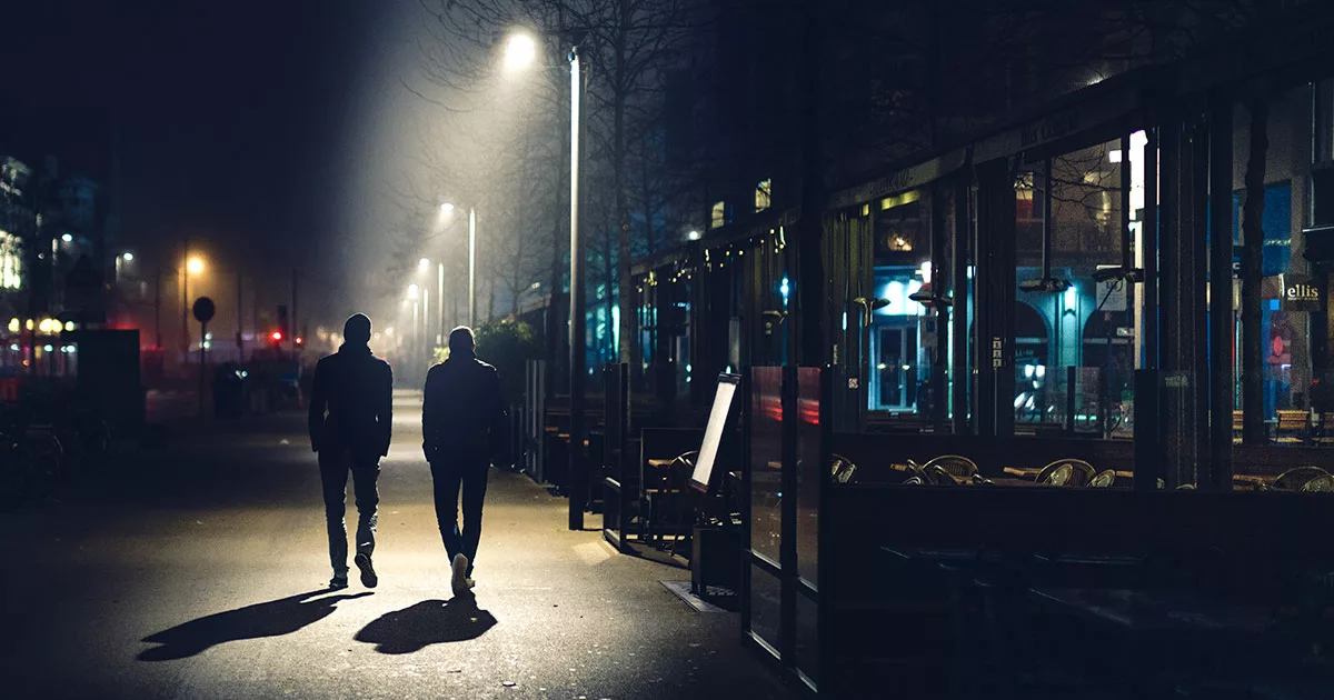 Two people walking at night in a lit urban street with storefronts