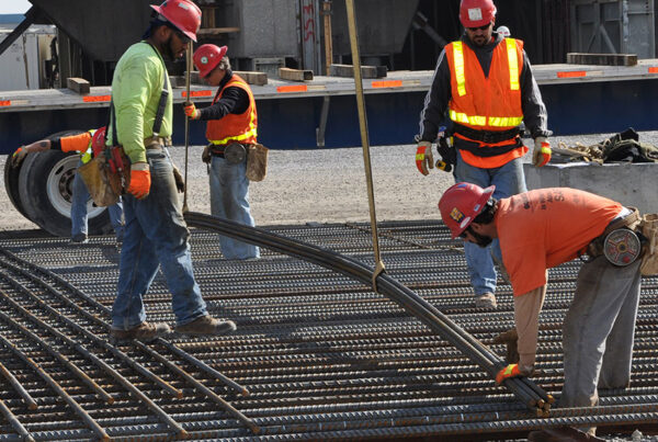 Construction workers in safety gear bending rebar at a construction site