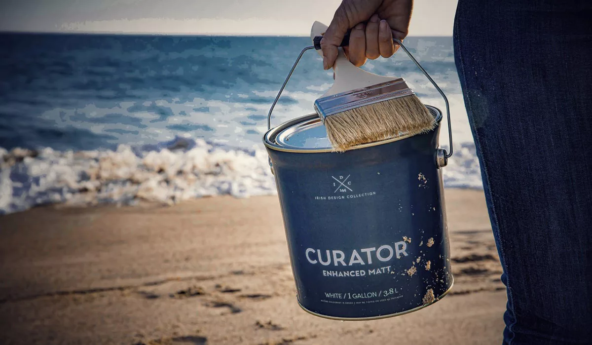 Hand holding paintbrush over bucket with ocean background