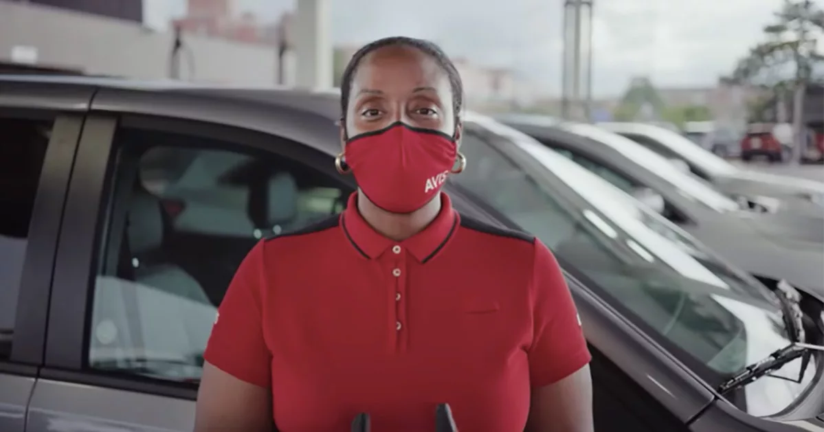 Woman in red shirt and mask standing in front of parked cars