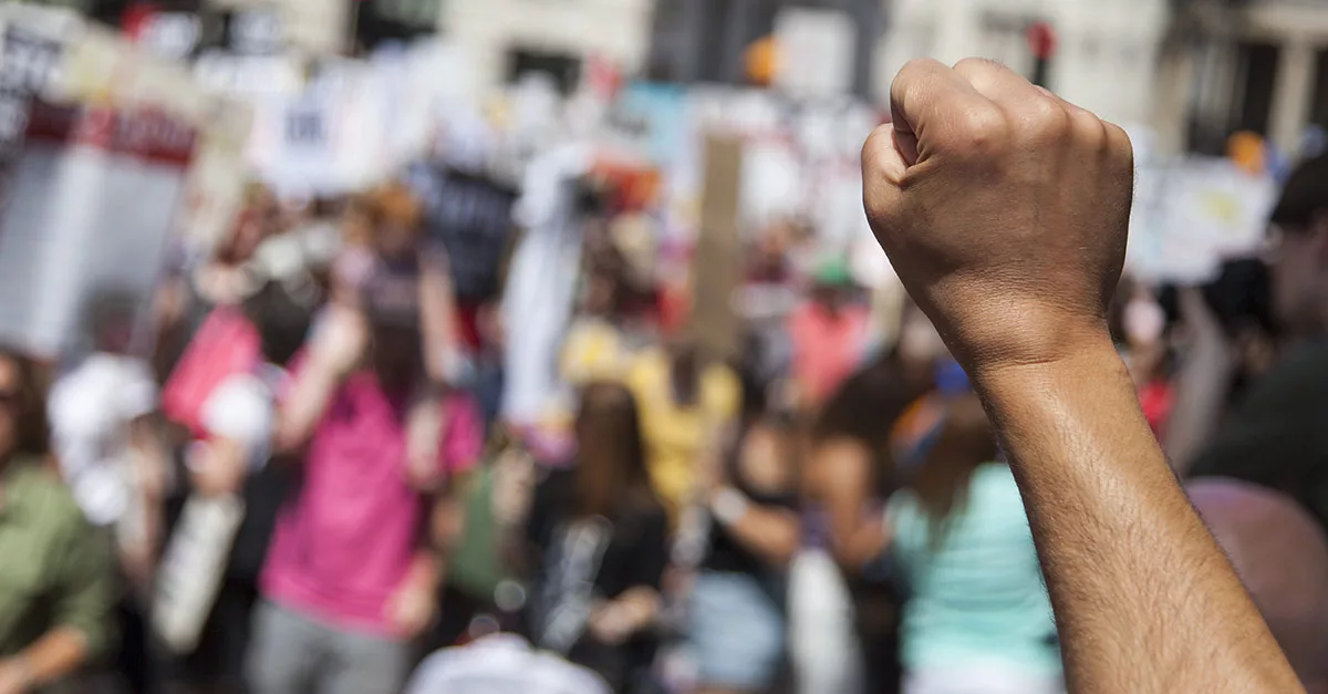 Raised fist in focus during protest with blurry crowd background
