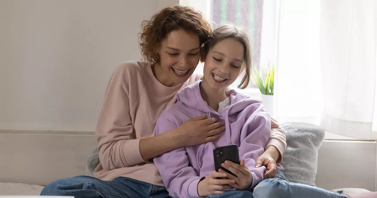 Two women smiling and looking at smartphone together indoors