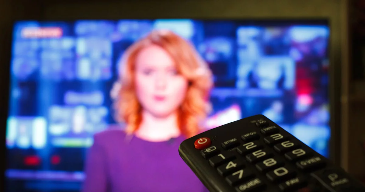 Blurred news anchor on TV screen with a sharp remote control in foreground