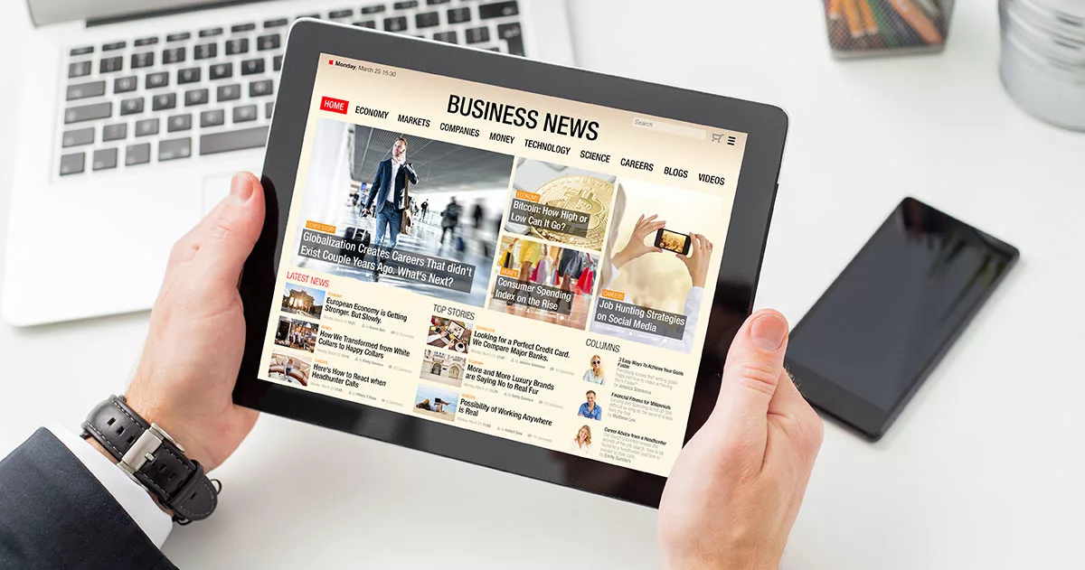 Person holding tablet displaying business news website with articles on economy and markets.