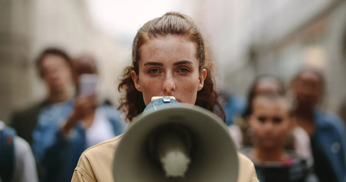 Woman with megaphone leading protest with blurred crowd in background