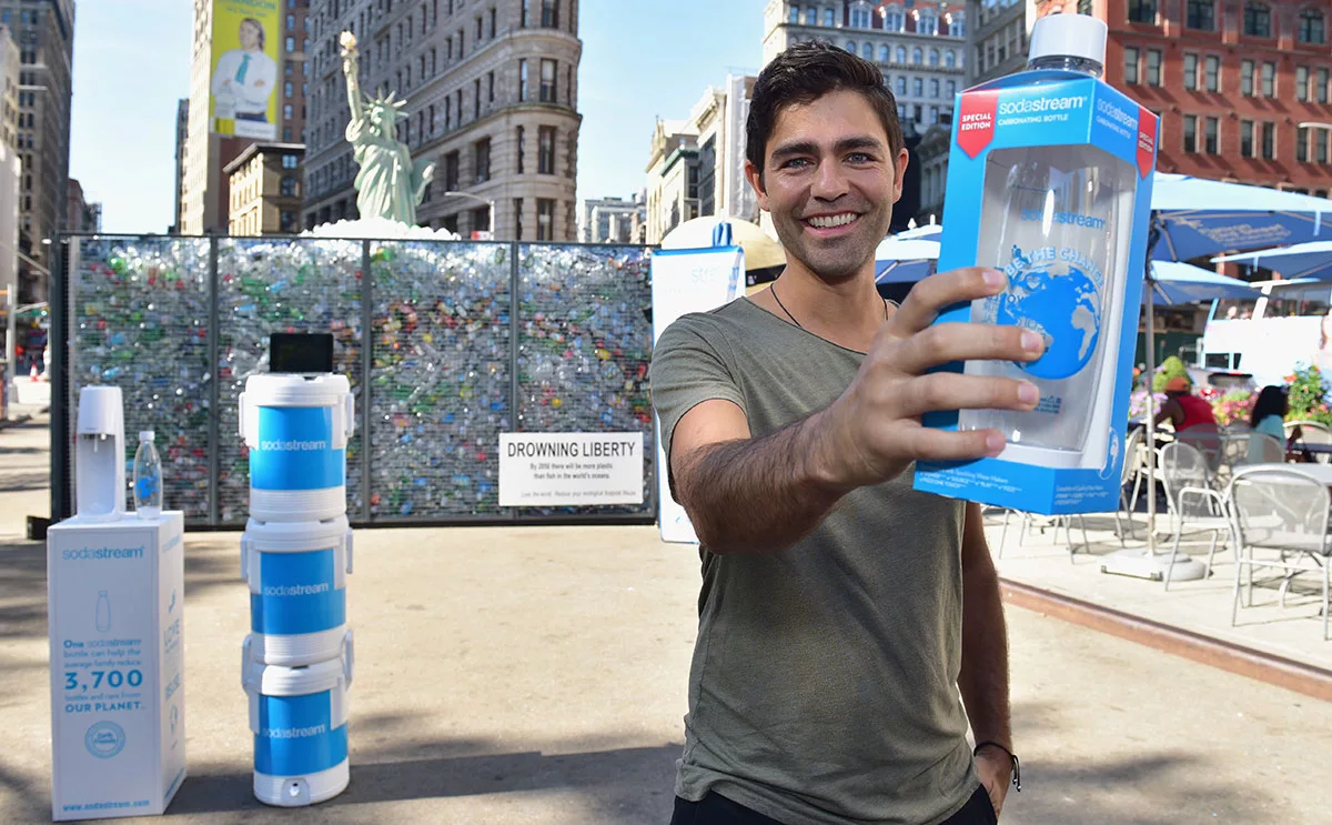 Man holding SodaStream bottle at event with recycling display in background