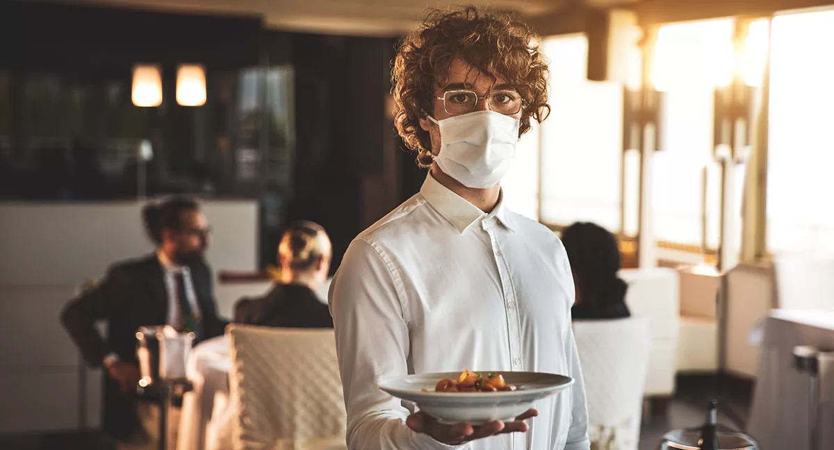 Waiter in mask serving food in a modern restaurant setting