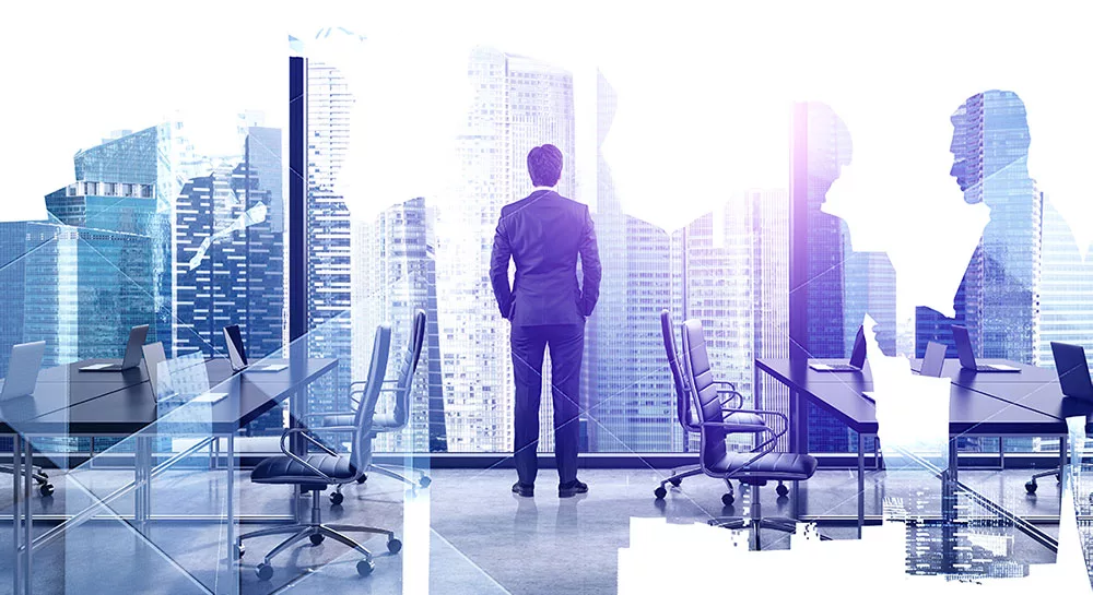 Businessman in office overlooking city skyline with silhouettes of colleagues